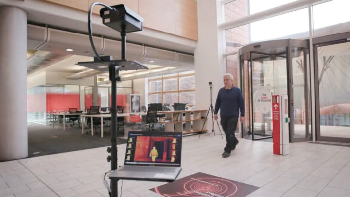 A person entering building and walking past thermal camera for temperature check.