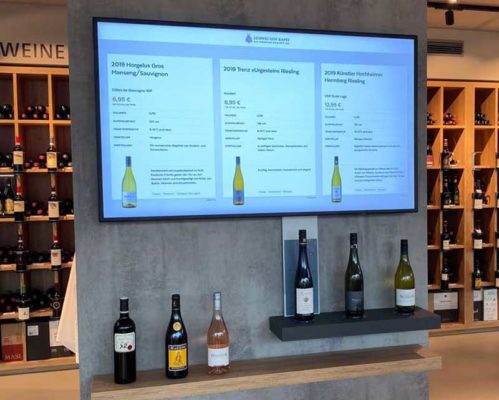 A wine store displays bottles of wine with in-depth information presented on a digital sign, improving the in-store experience for its customers.